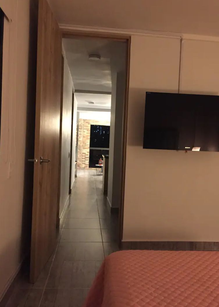 Een hotelgangen met een bed, een aan de muur bevestigde televisie en een deur naar een andere kamer.