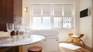 Una cocina moderna con encimera de mármol, un comedor con sofá blanco y sillas de madera, y un amplio ventanal con persianas.