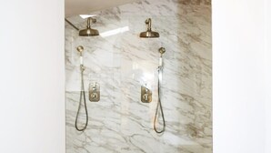 Un baño moderno con pared de ducha de mármol, dos cabezales de ducha y zona de ducha con mampara de cristal.