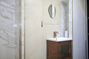 A bathroom with a marble wall, a wooden vanity, a sink with a gold faucet, and a mirror.