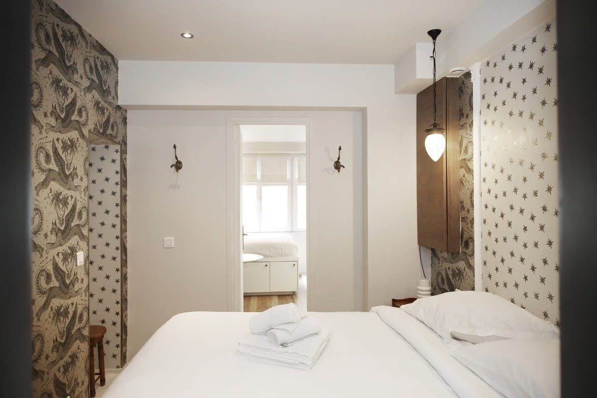 Een hotelkamer met een bed, nachtkastje, een wandlamp en een deur naar een badkamer.