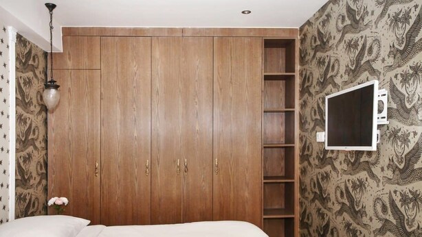 Un dormitorio con un armario amplio, una cama, un televisor en la pared y papel tapiz estampado.