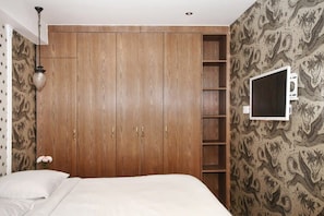 A bedroom with a large wardrobe, a bed, a TV on the wall, and patterned wallpaper.