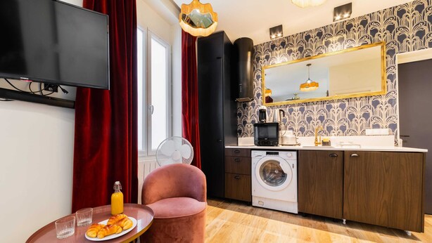 A compact kitchen with a washing machine, a dining area with a table and chair, and a large mirror above the counter. - Studio lumineux et moderne proche du metro - 2P (Paris)