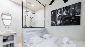 A modern hotel room with a white bed, a large mirror, a shower with gold fixtures, and a black and white artwork on the wall. - Studio lumineux et moderne proche du metro - 2P (Paris)
