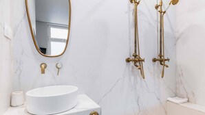 A bathroom with a white sink, gold fixtures, and a marble wall. - Studio lumineux et moderne proche du metro - 2P (Paris)