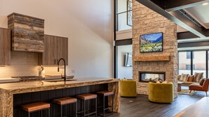 A modern kitchen with a stone wall, a large island with stools, and a fireplace. - Eagles View- Perfect location near downtown Cody, New Luxury Family Condo (Cody)