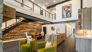 A modern interior with a wooden accent wall, a staircase, a kitchen area, and green upholstered chairs. - Eagles View- Perfect location near downtown Cody, New Luxury Family Condo (Cody)