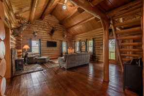 A log cabin interior with a wooden ceiling, a fireplace, a sofa, and mounted deer heads. - Cozy Cabin- Classic Log Cabin, Great Location close to Cody! (Cody)