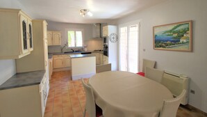 A kitchen with a dining area, a clock, and a painting on the wall.