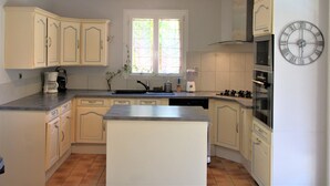 A kitchen with white cabinets, a central island, a built-in oven, and a clock on the wall.