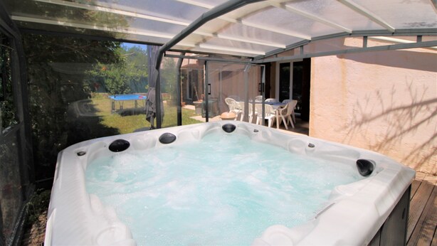 A hot tub with a glass enclosure, surrounded by a wooden deck and a patio area with outdoor furniture.
