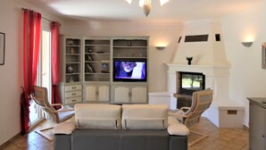 A living room with a sofa, two armchairs, a television, a fireplace, and a bookshelf.