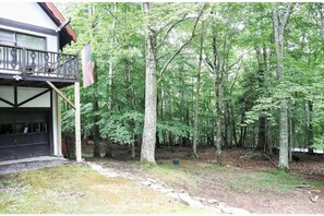 A two-story building with a balcony and a garage, surrounded by a dense forest.