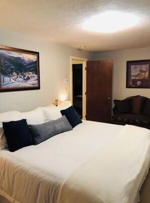 A hotel room with a bed, a nightstand, a lamp, a door, and a chair.