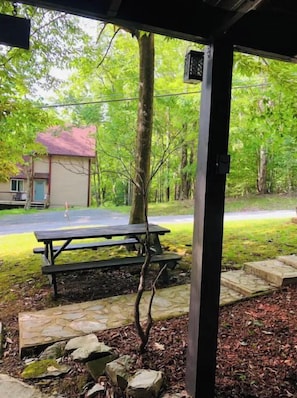 A covered picnic area with a table and benches, surrounded by a stone pathway and a small tree.