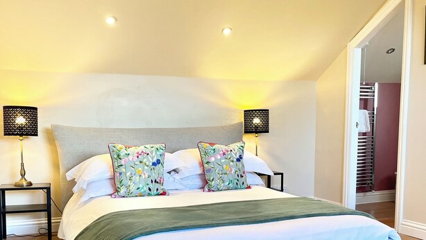 A modern bedroom with a large bed, two bedside lamps, a fluffy rug, and a view of a staircase. - Inviting Townhouse in Bedlington (Bedlington)