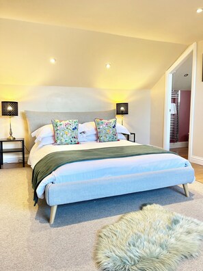 A modern bedroom with a large bed, two bedside lamps, a fluffy rug, and a view of a staircase. - Inviting Townhouse in Bedlington (Bedlington)