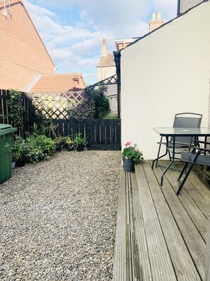 A wooden deck with a table and chairs, surrounded by a gravel area and a black fence. - Inviting Townhouse in Bedlington (Bedlington)