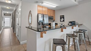 Cocina moderna con una isla central, taburetes de bar, armarios de madera y electrodomésticos de acero inoxidable, con vista al pasillo.
