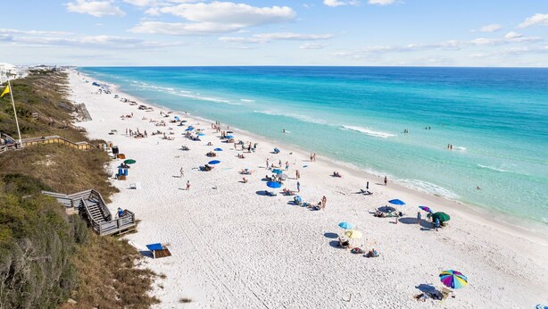 Una playa con agua turquesa cristalina, arena blanca y varios sombrillas.
