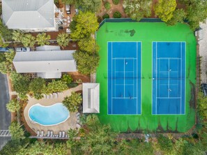 An aerial view of a property with a tennis court, a swimming pool, and surrounding greenery.