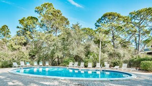 Una piscina con sillas de descanso y árboles al fondo.