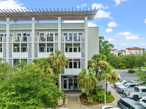 A multi-story building with balconies, a covered parking area, and lush greenery.