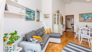 Ein modernes Wohnzimmer mit einem grauen Ecksofa, einem Essbereich mit weißen Stühlen und einem Holzboden im Fischgrätmuster.