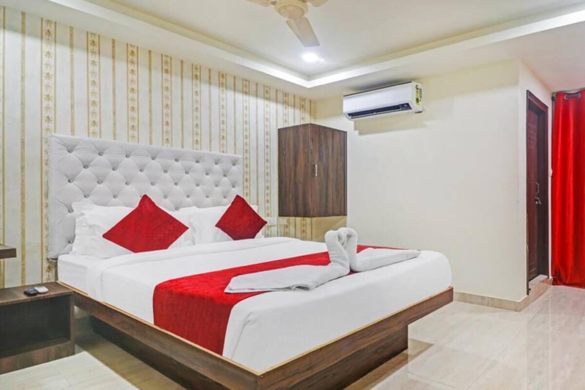 Une chambre d’hôtel avec un grand lit, une tête de lit en bois, une armoire, un climatiseur et un rideau rouge.