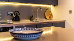 A modern kitchen with a built-in dishwasher, a kettle, a sink, and a wooden cutting board. - No. 35 (York)