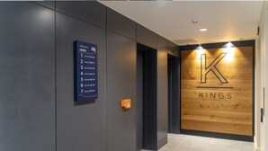 A modern hotel lobby with a dark grey wall, a sign listing apartment numbers, and a wooden wall with the hotel's logo. - No. 35 (York)