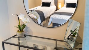 A hotel room with a bed, a bedside table with a vase of white orchids, and a round mirror reflecting the room. - No. 35 (York)