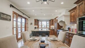 Un comedor con una mesa de madera dispuesta para cuatro personas, rodeado de armarios de madera y una cocina al fondo.