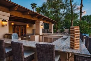 An outdoor kitchen area with a stone countertop, wicker furniture, and a chimney.