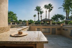 An outdoor patio area with stone countertops, a seating area, and palm trees in the background.