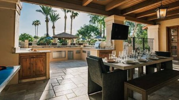 Un área de comedor al aire libre con piscina, techo de madera y vistas a palmeras.