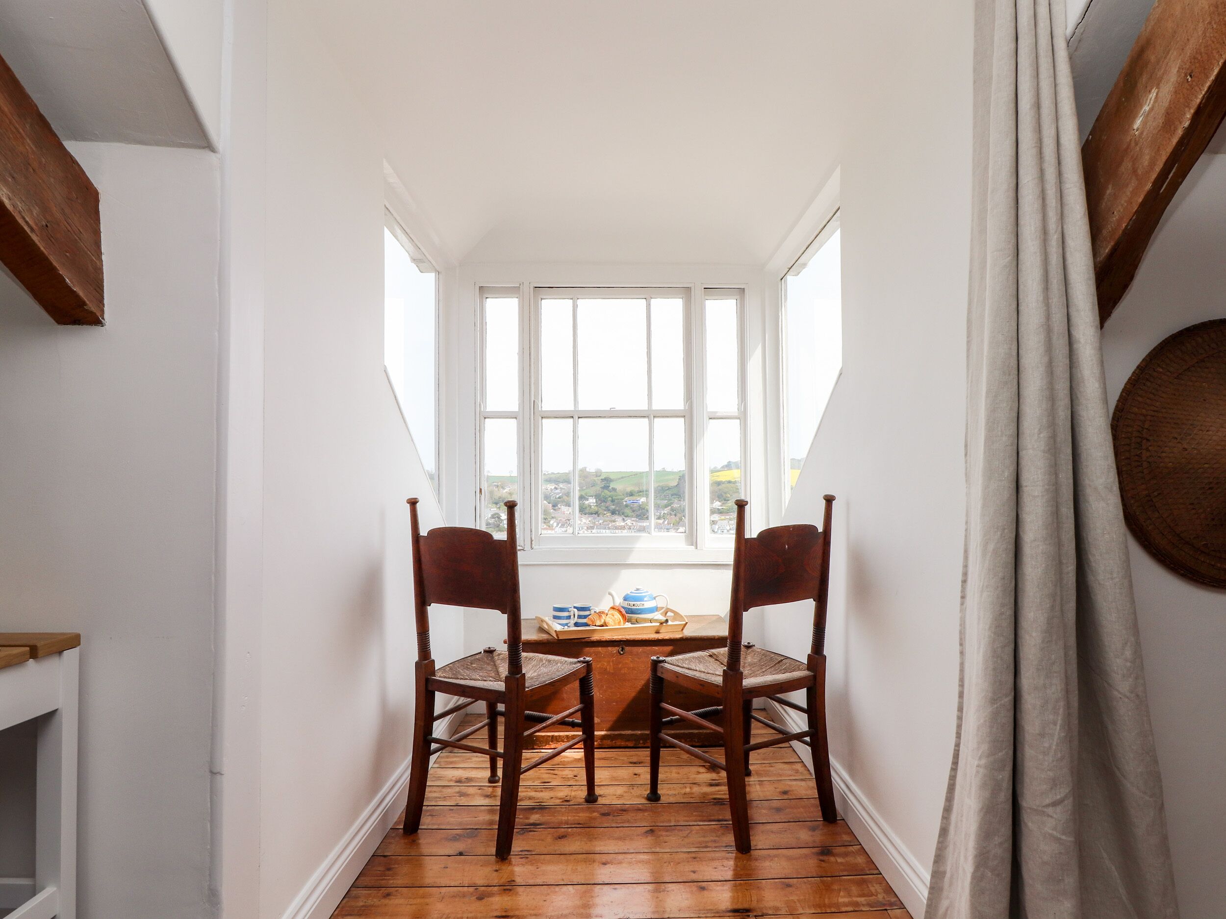 A narrow room with two wooden chairs and a table, large windows, and a view of the outside.