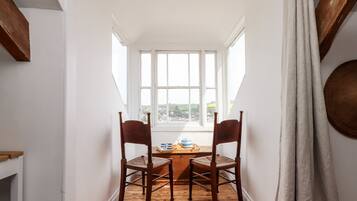 A narrow room with two wooden chairs and a table, large windows, and a view of the outside.