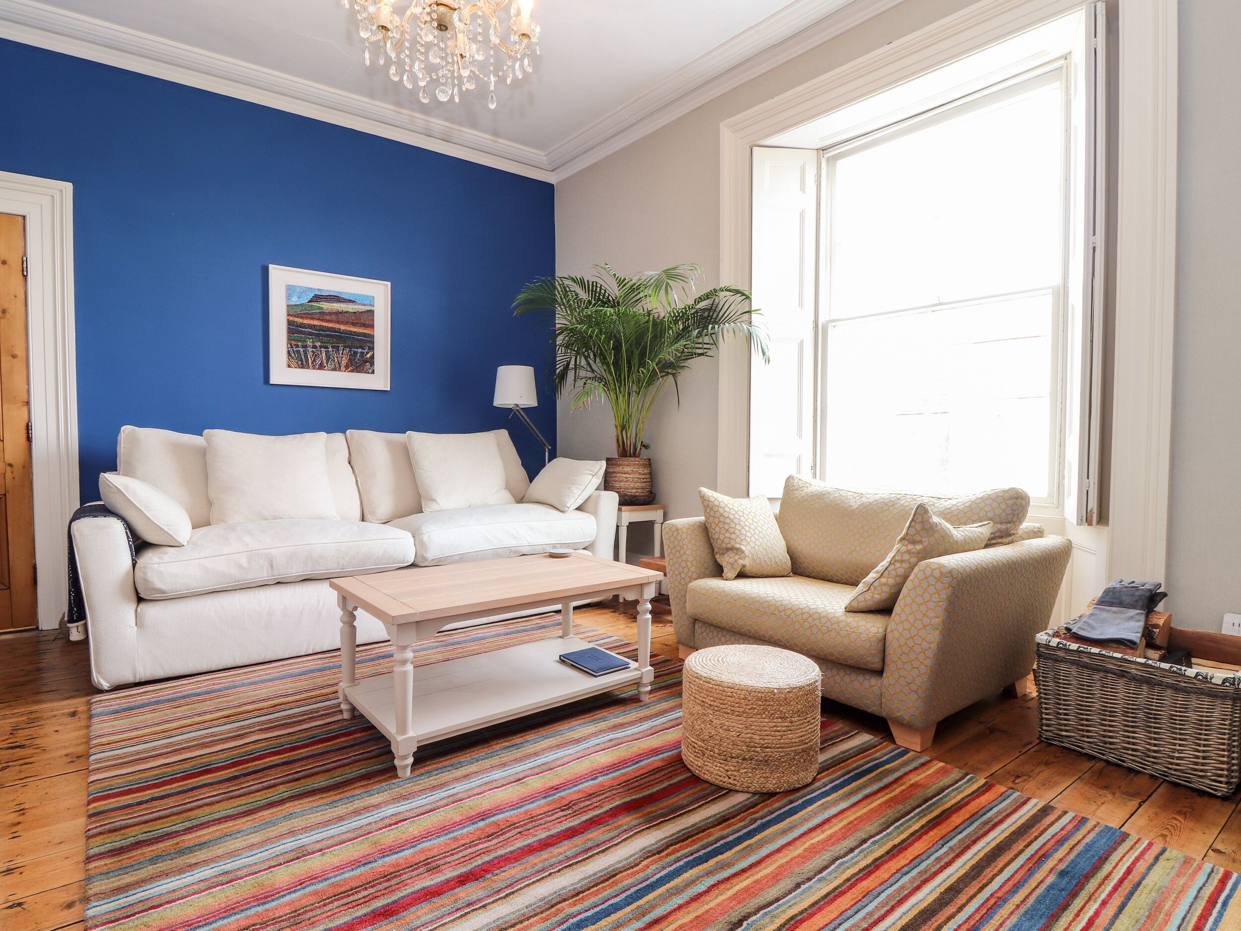 A living room with a white sofa, a beige armchair, a coffee table, a striped rug, and a large window.