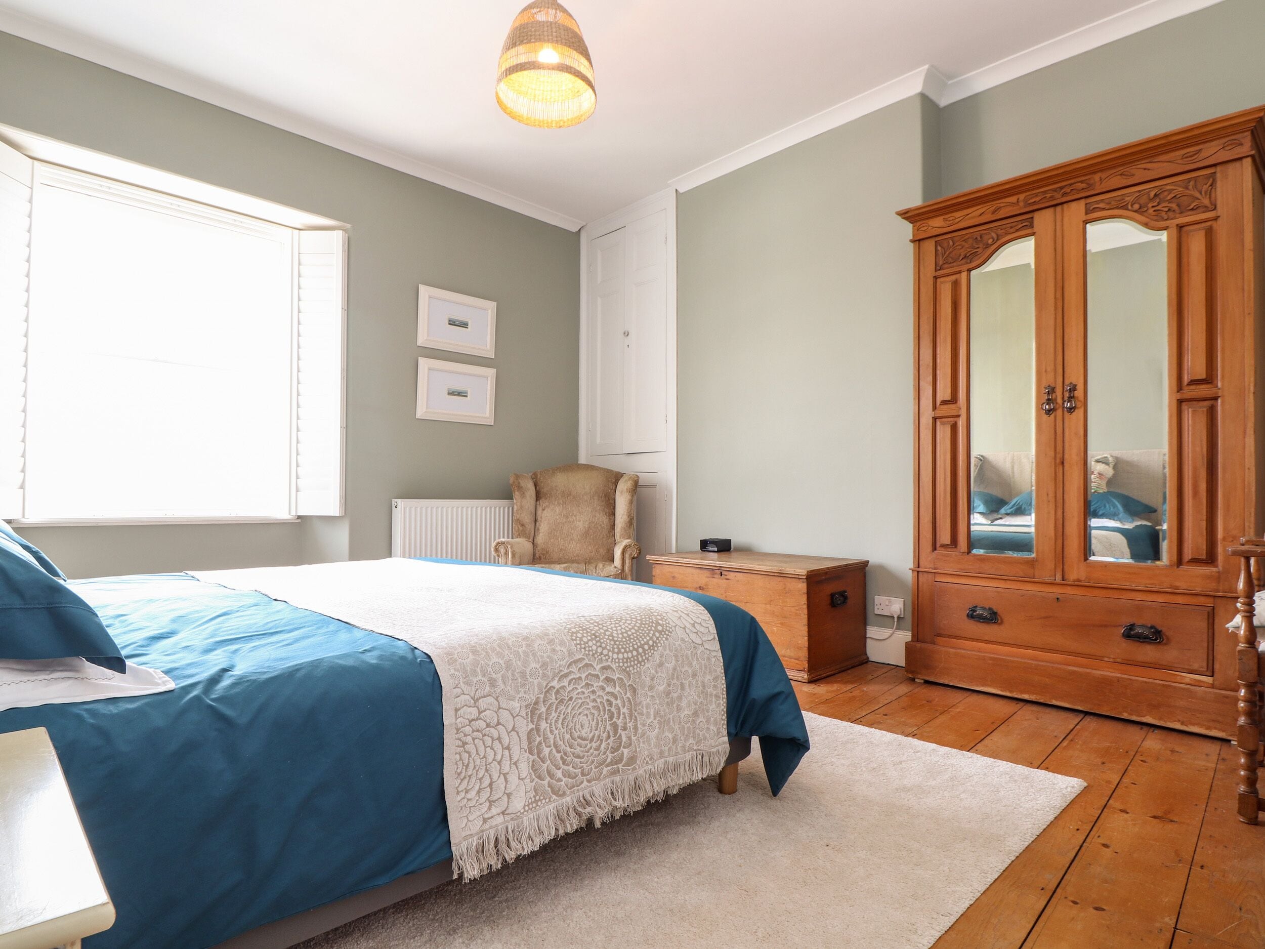 A bedroom with a bed, a wooden wardrobe, a chair, and a radiator.