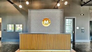 A reception desk with a logo, a grey textured wall, and a wooden floor.