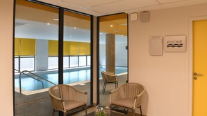 A room with two wicker chairs, a small table with a decorative glass bowl, and a view of an indoor swimming pool through large glass doors. - Domitys - Regalecia (Uzès)