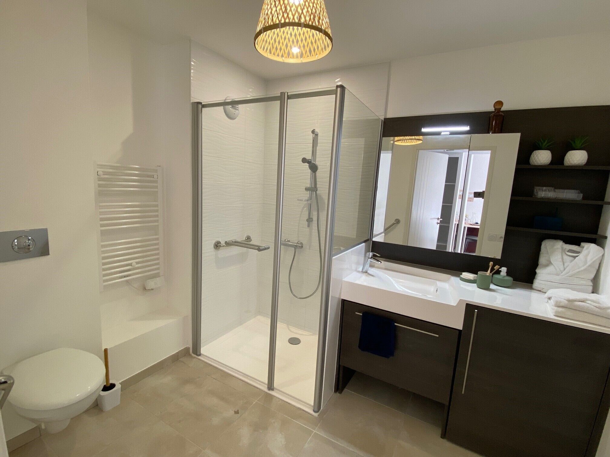 Un baño moderno con ducha envuelta en vidrio, inodoro blanco, tocador con espejo y toallero.
