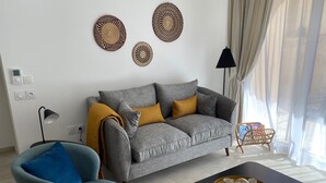 A living room with a grey sofa, a blue armchair, a black coffee table, and decorative woven items on the wall. - Domitys - Regalecia (Uzès)