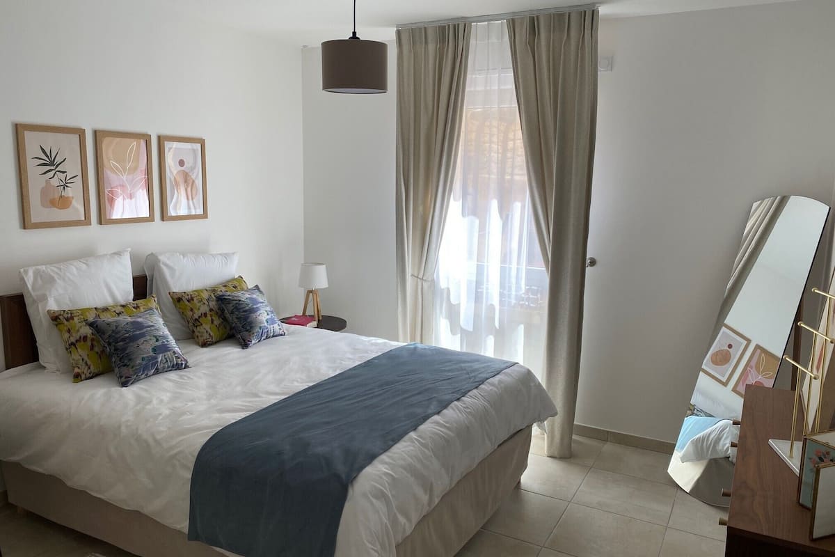 Un dormitorio con una cama grande, una mesita de noche con lámpara y un espejo en la pared.
