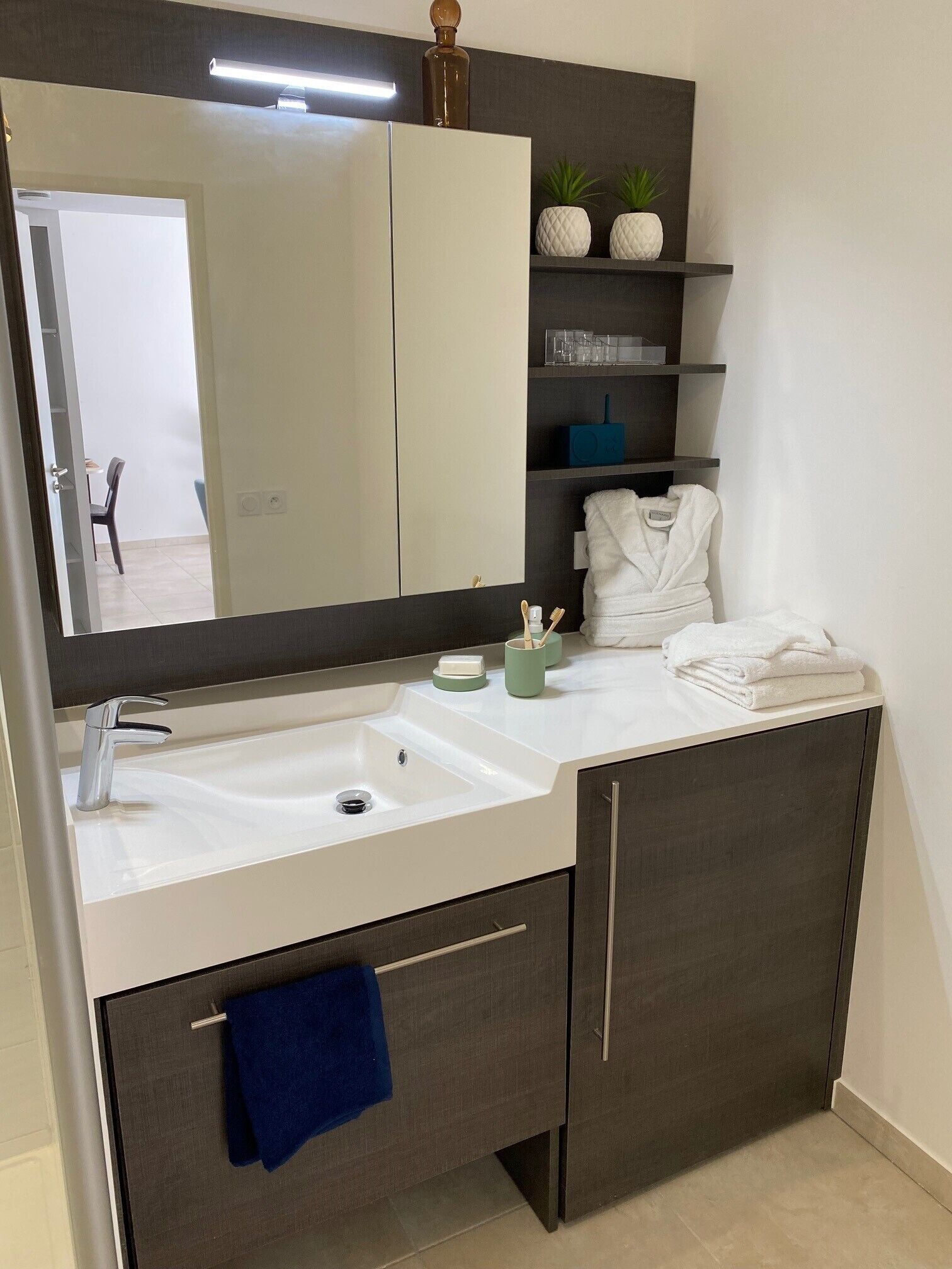 A modern bathroom with a large mirror, a white sink, dark cabinets, and a towel rack.