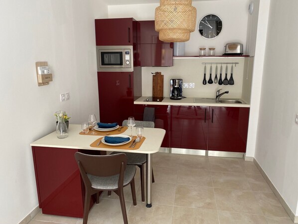 Una cocina compacta con microondas, cafetera y utensilios colgando en la pared.