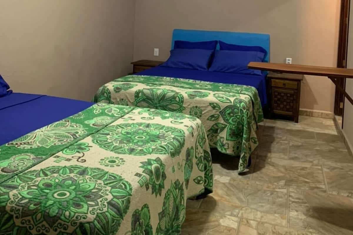 A room with two beds, a ceiling fan, a painting on the wall, and a tiled floor.