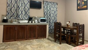 A compact kitchen with a microwave, toaster, and coffee maker on the counter, wooden cabinets, and a dining table with chairs. - Bungalows Victoria (La Manzanilla)